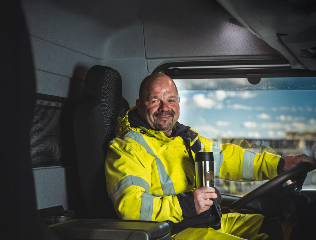 LKW-Fahrer von Meyer Entsorgung sitzt im Fahrerhaus eines modernen LKW und hält einen Kaffeebecher