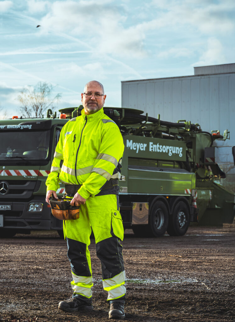 Mitarbeiter von Meyer Entsorgung in Warnschutzkleidung steht vor einem Spezialfahrzeug auf dem Betriebshof und hält eine Steuerung in der Hand